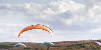 Deux parapentes en vol au-dessus d'un relief verdoyant, sous un ciel bleu parsemé de cumulus