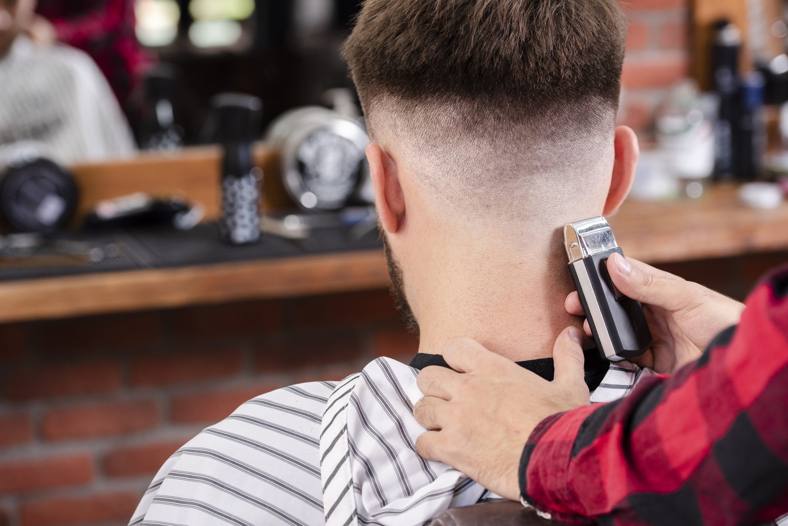 Barbier réalisant un dégradé taper sur la nuque d'un client à la tondeuse